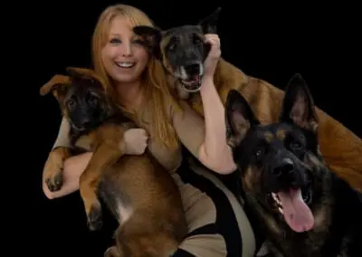 Woman smiling holding three Belgian Malinois dogs for WestInn Kennels.