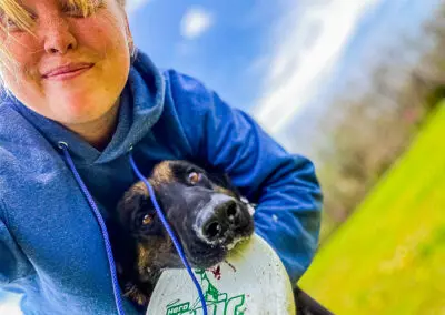 Woman in blue hoodie hugging dog holding a frisbee in grass