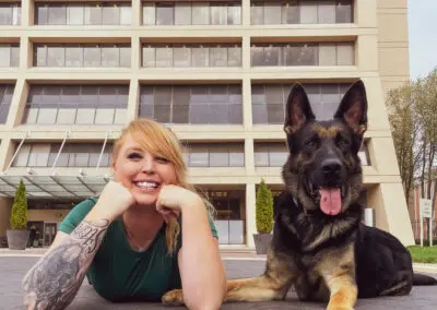 Woman smiling on plaza with German shepherd sitting beside her